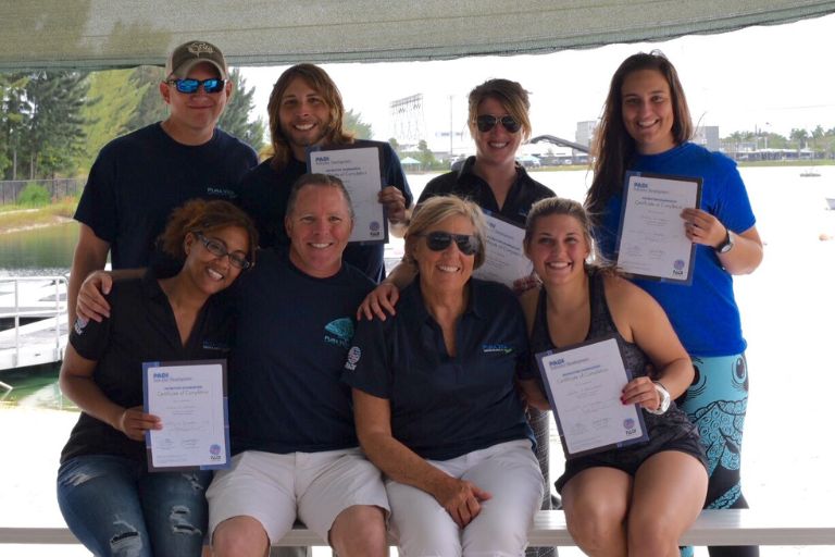 New PADI Instructors celebrate with their course directors, holding their Instructor certificates and smiling