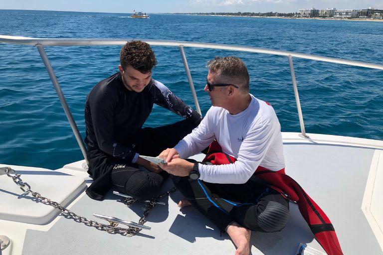A dive instructor and their student discuss their dive plan on the bow of a boat in the ocean