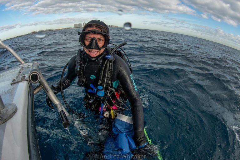 A smiling diver climbs the ladder on the back of a boat as she gets out of the water after a dive in her Instructor Development Course